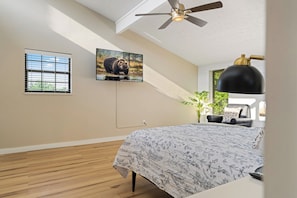 Un dormitorio con cama, ventilador de techo, televisor y ventana con persianas.