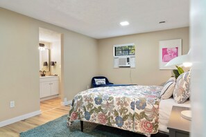 Une chambre à coucher comprenant un lit, une commode, un miroir, une fenêtre avec des stores et un climatiseur fixé au mur.