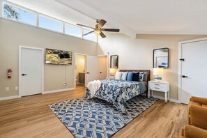 A bedroom with a bed, a nightstand, a mirror, a ceiling fan, and a window.