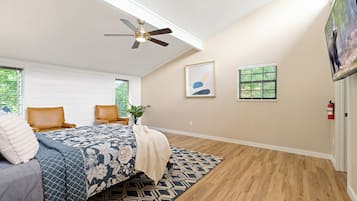 A bedroom with a bed, two chairs, a ceiling fan, a window, and a fire extinguisher.