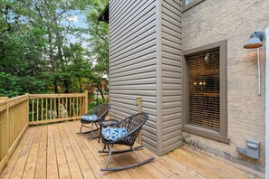 Een houten terras met twee schommelstoelen en een raam met zonwering.