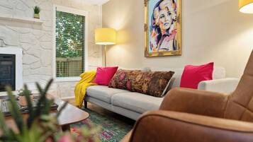 A living room with a stone wall, a fireplace, a sofa with colorful cushions, a floor lamp, and a painting on the wall.
