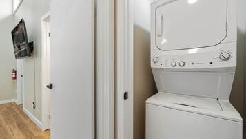 A laundry room with a white washing machine, a fire extinguisher, and a wall-mounted television.