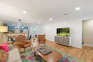 Een moderne woonkamer met een televisie, twee leren fauteuils, een salontafel en een keuken op de achtergrond.