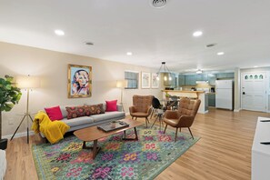 A modern living room with a sofa, coffee table, and chairs, a dining area with a table and chairs, and a kitchen with appliances.