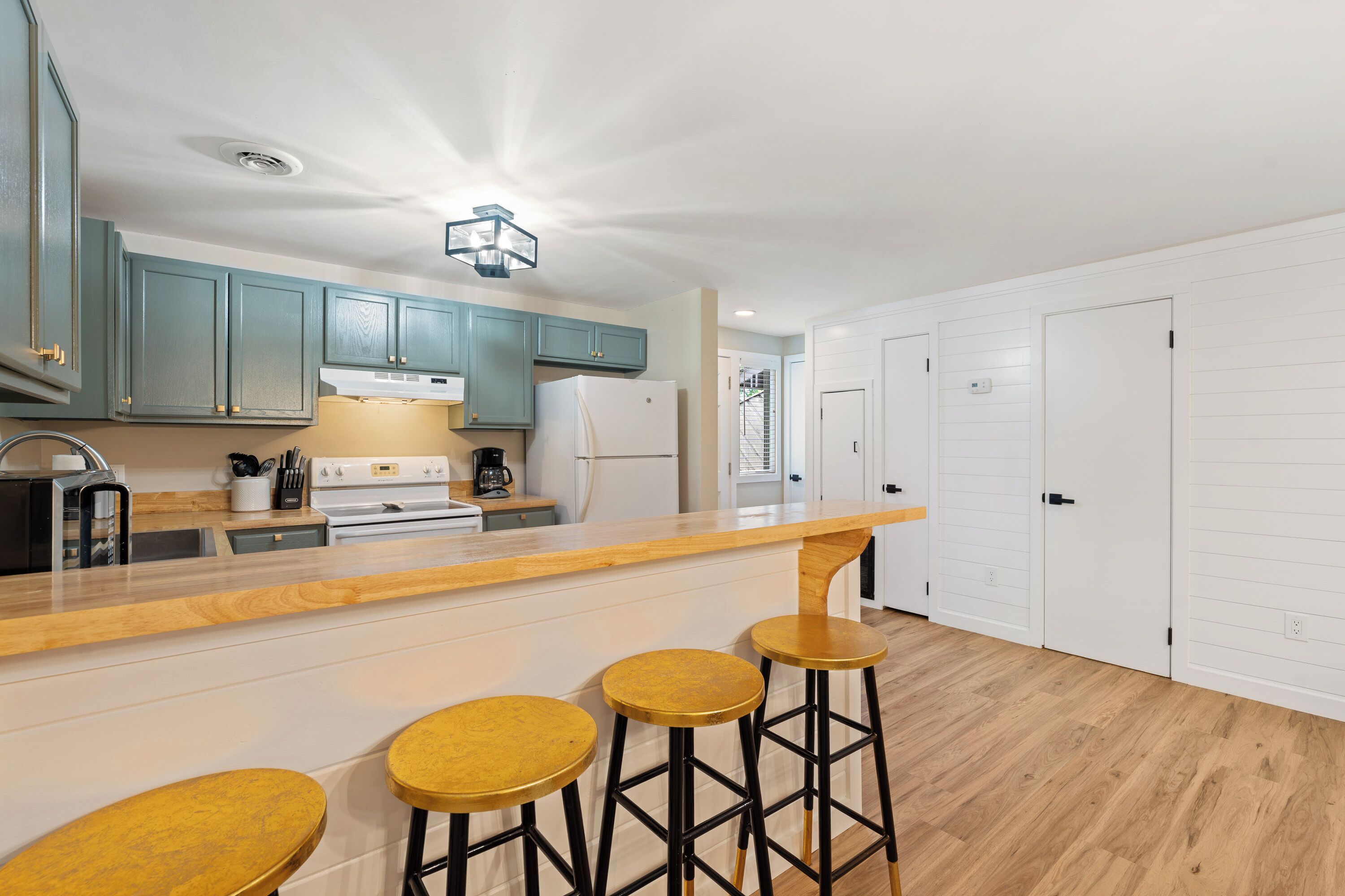 Una cucina moderna con mobili color petrolio, un piano di lavoro bianco e un'area bar con sgabelli.