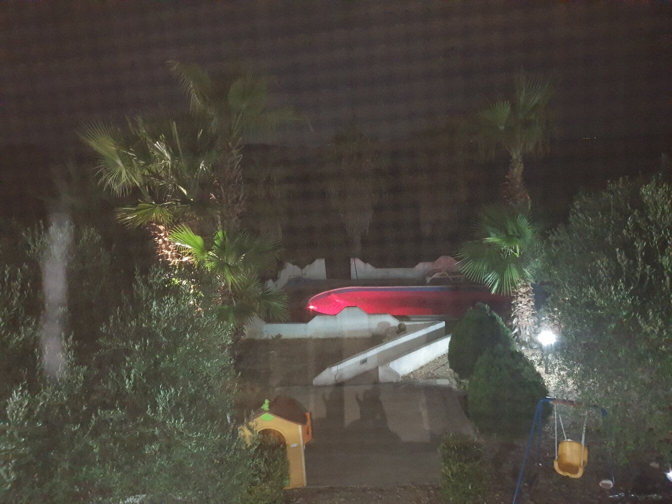 A nighttime view of a model train set in a garden with palm trees and a small birdhouse.