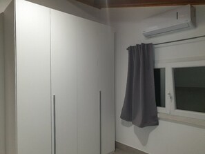 A room with a wardrobe, a window with curtains, and an air conditioning unit.