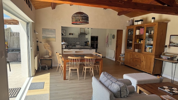 Een ruime woonkamer met een houten eettafel, een gestreepte bank en een keuken op de achtergrond.