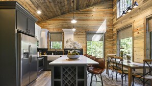 Een moderne keuken met een centraal eiland, roestvrijstalen apparatuur en een eethoek met houten tafels en stoelen.