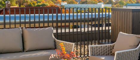 A terrace with a sofa, chairs, and a table, overlooking a river and buildings.