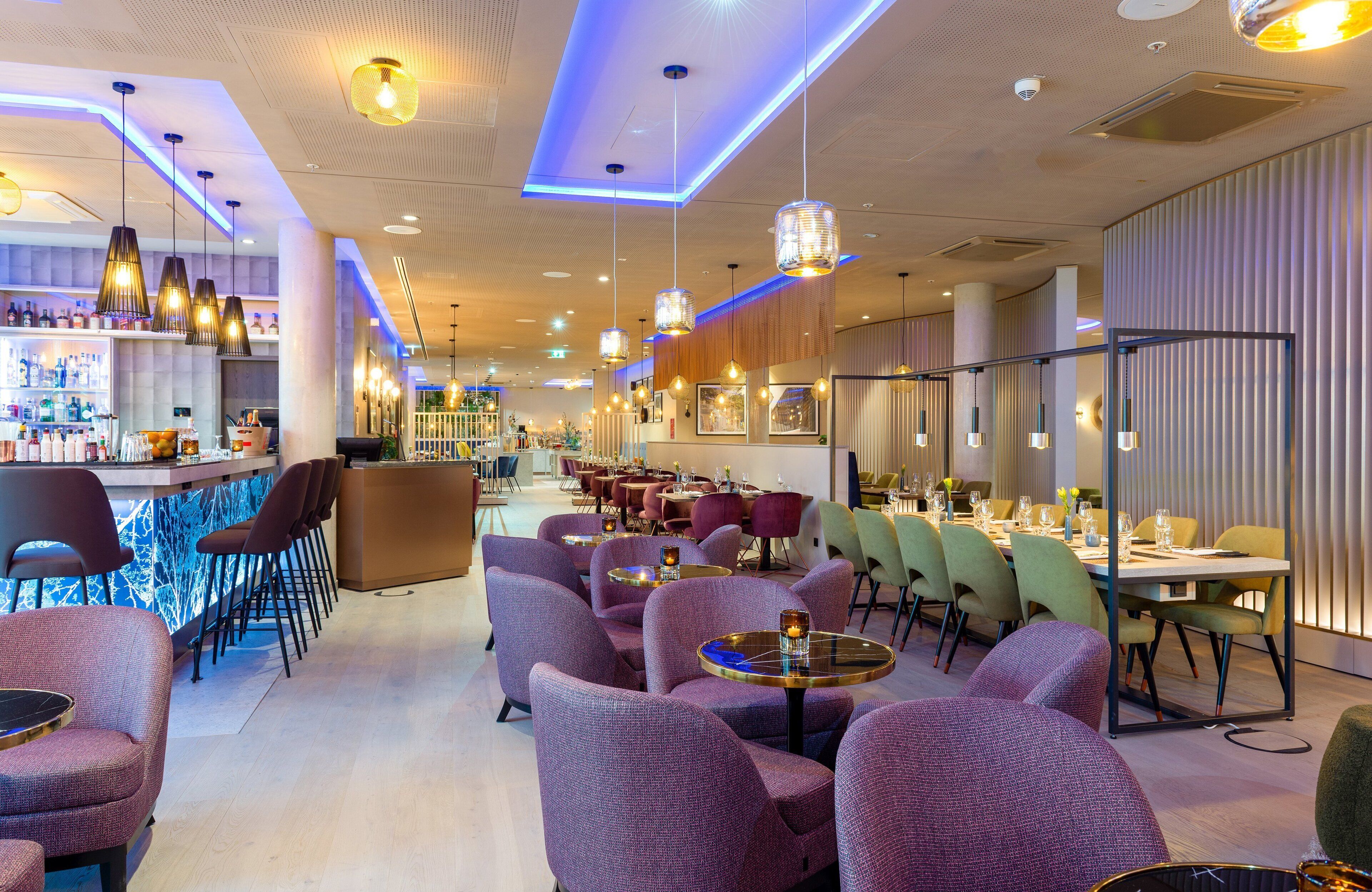 Un restaurante moderno con sillas tapizadas de color púrpura, mesas redondas e iluminación colgante.