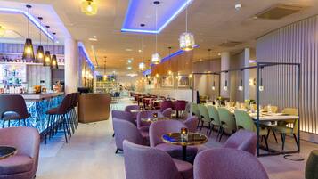 Un restaurante moderno con sillas tapizadas de color púrpura, mesas redondas e iluminación colgante.