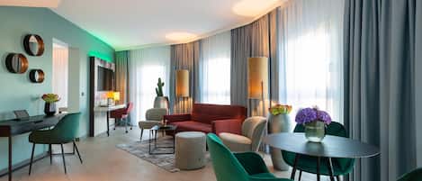 Un salon moderne avec un canapé rouge, des fauteuils verts, une table ronde et un bureau avec un ordinateur.