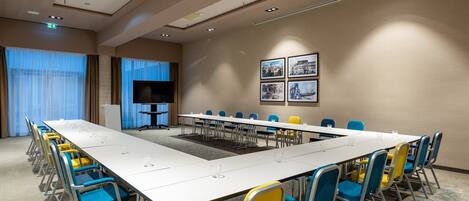 A conference room with a long table, blue and yellow chairs, a flat-screen TV, and framed pictures on the wall.
