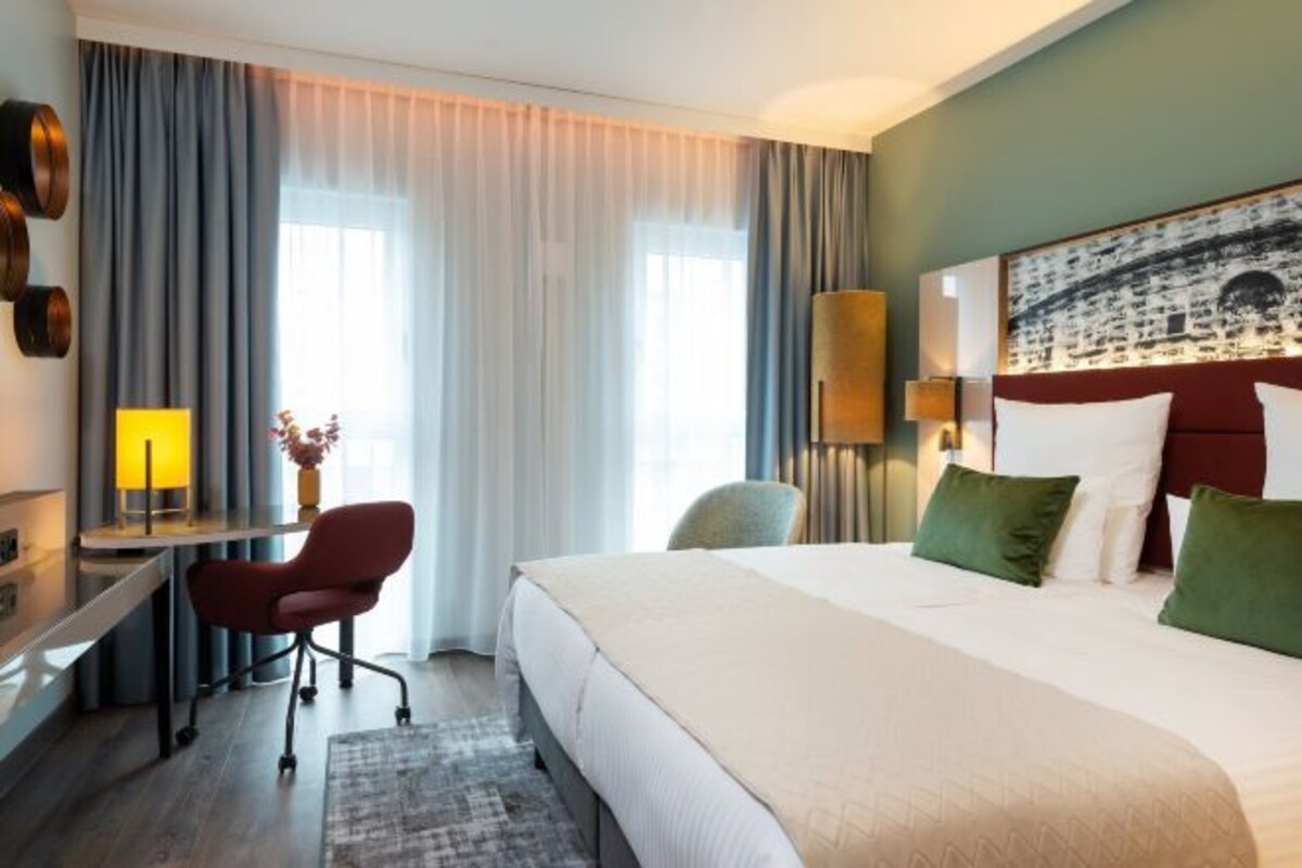 Habitación de hotel con una cama grande, un escritorio, una silla y vistas al exterior a través de la ventana.
