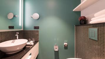 Un baño con un lavamanos grande tipo recipiente, un espejo, un perchero para toallas y un inodoro.