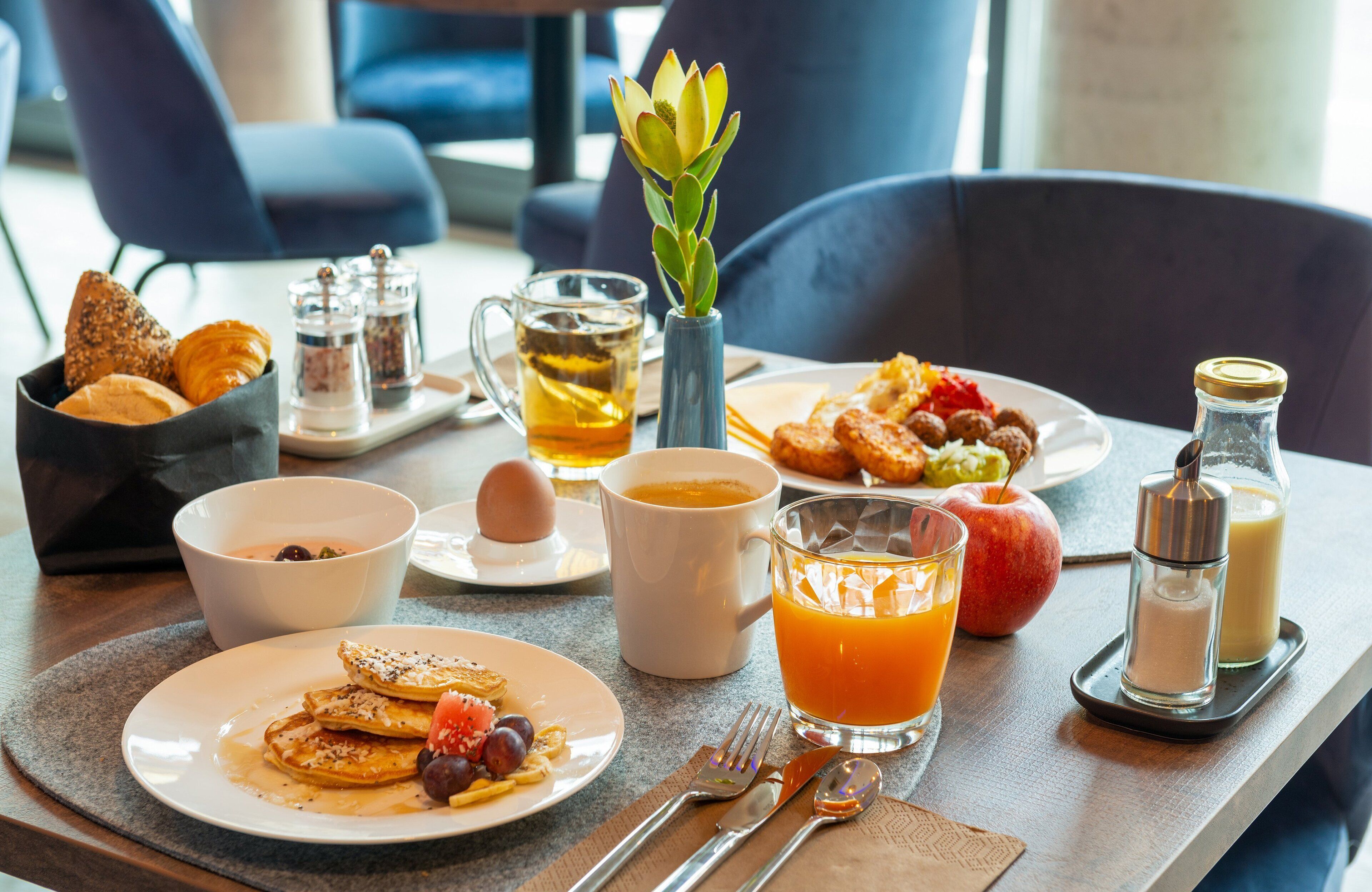 A breakfast setting with various dishes, drinks, and condiments on a table.