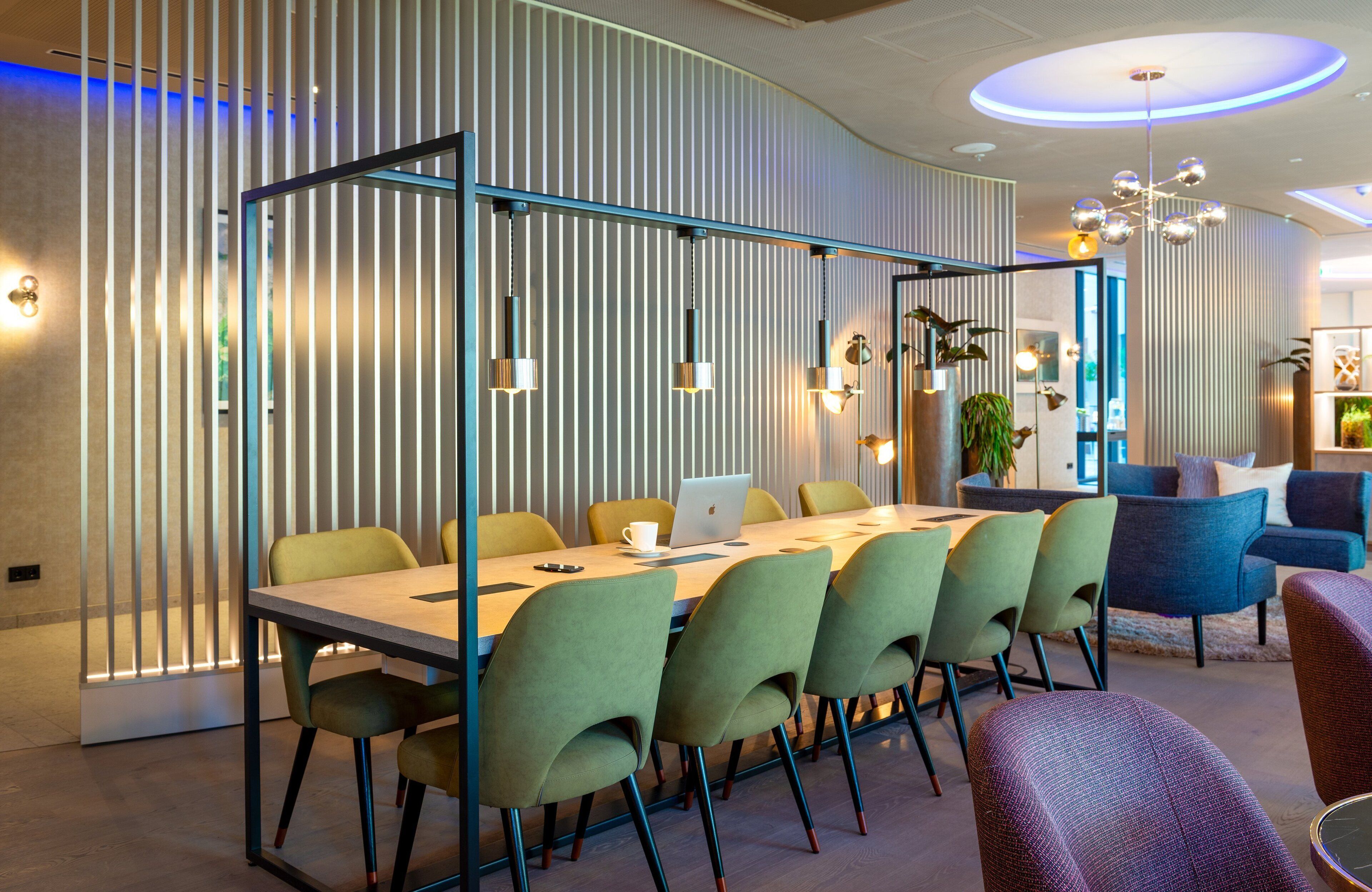 A modern meeting room with a long table, green chairs, and a laptop.