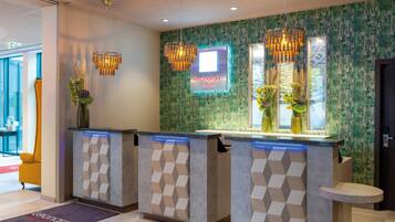 A hotel reception area with a modern design, featuring a reception desk, a neon sign, and decorative lighting.