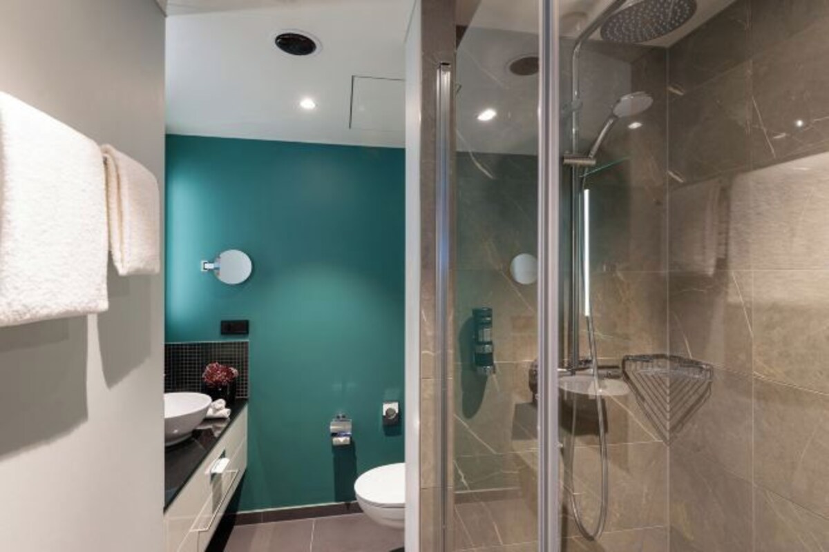 Un baño moderno con cabina de ducha de vidrio, lavamanos blanco y una pared de acento color aguamarina.
