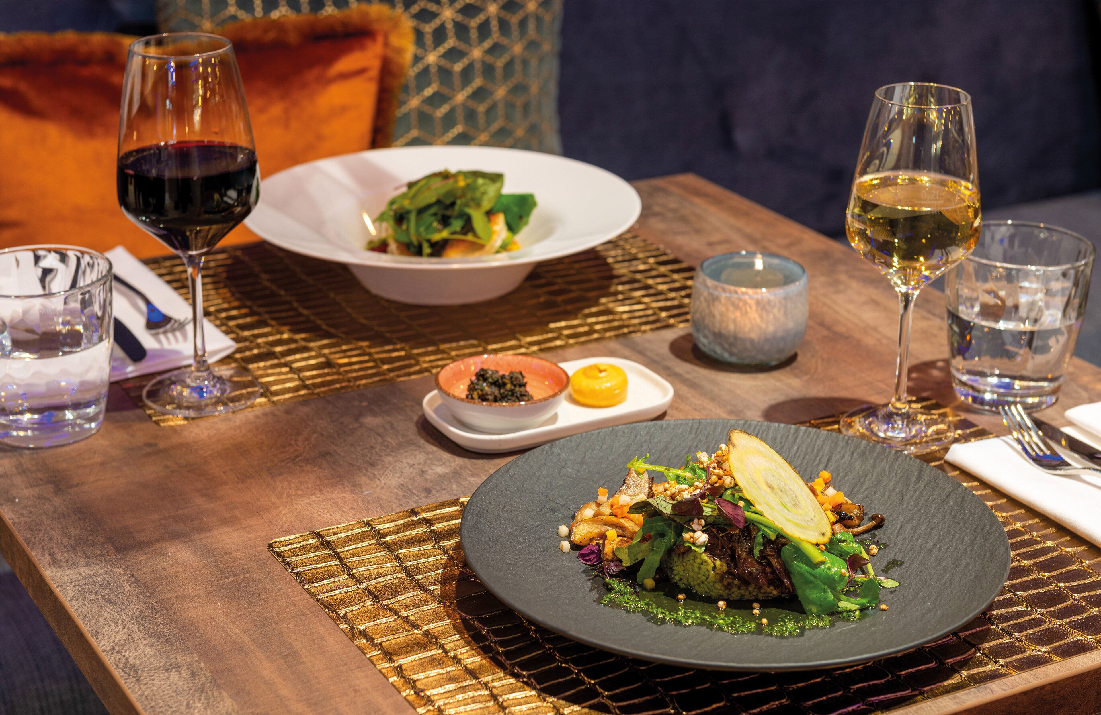 A dining table with two plates of food, two glasses of wine, and a candle.