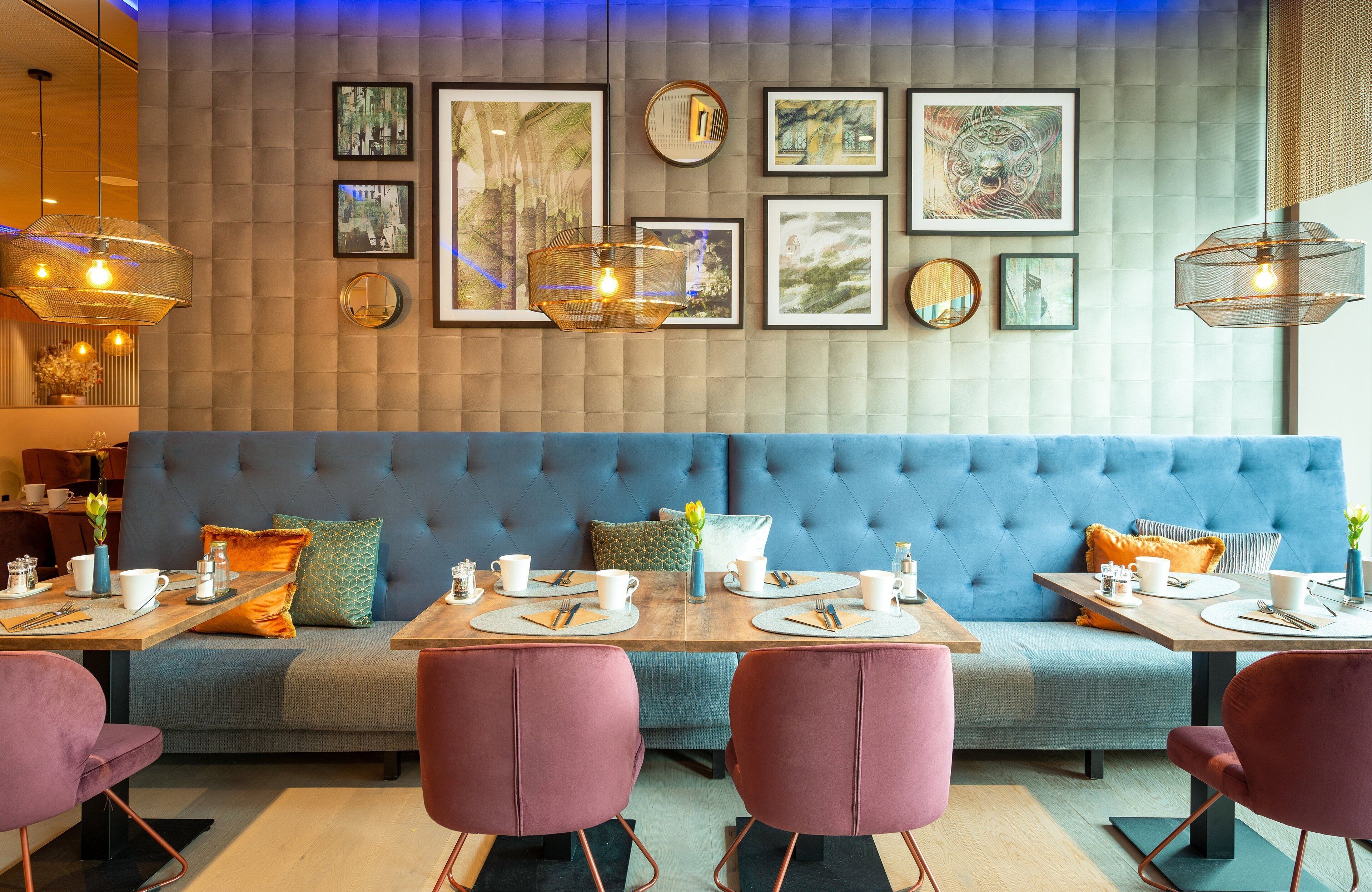 Un comedor moderno con un sofá tapizado en azul, sillas rosadas y una mesa de madera preparada para cuatro comensales.