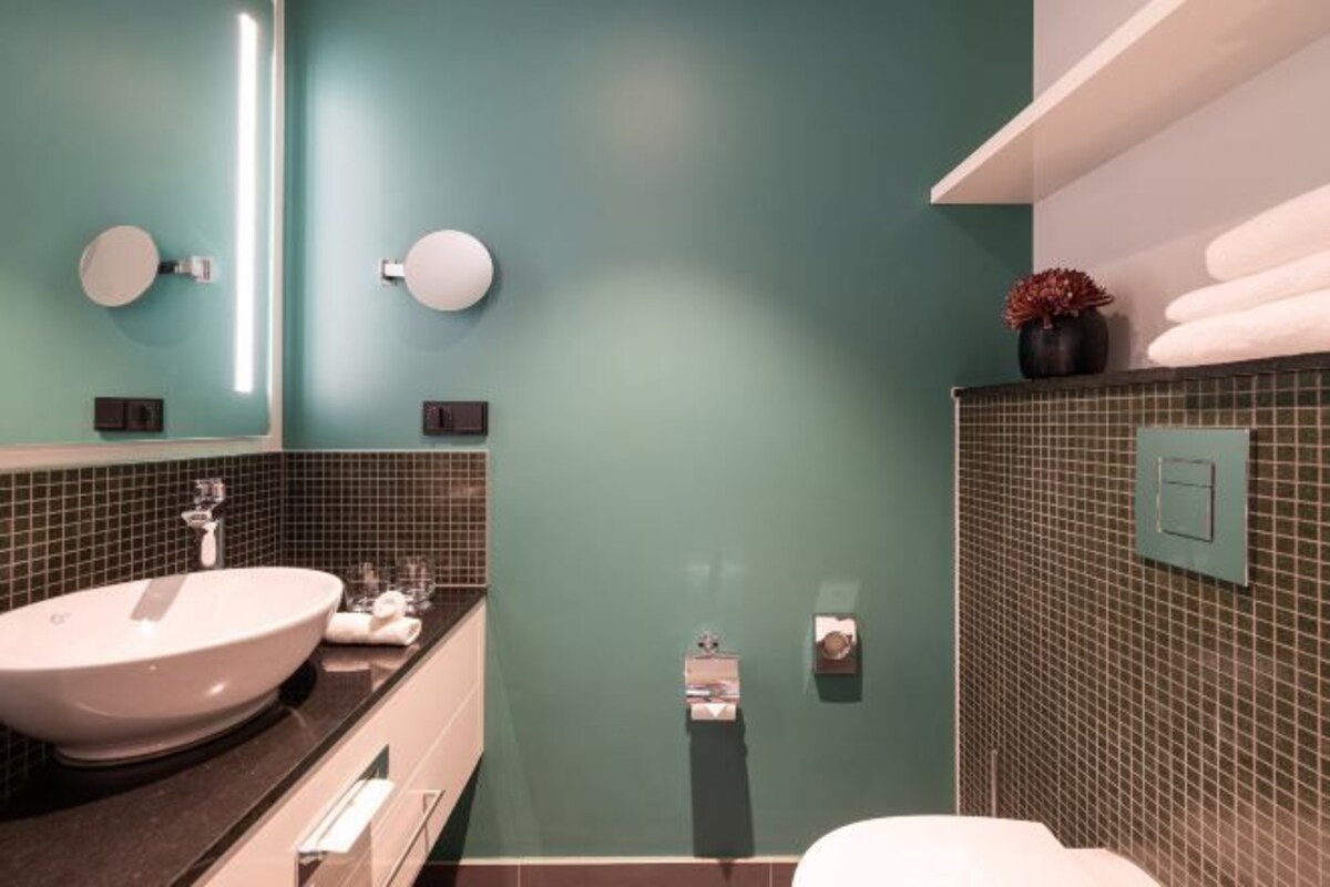 Un baño con un lavamanos grande, un espejo, un perchero para toallas y un inodoro.