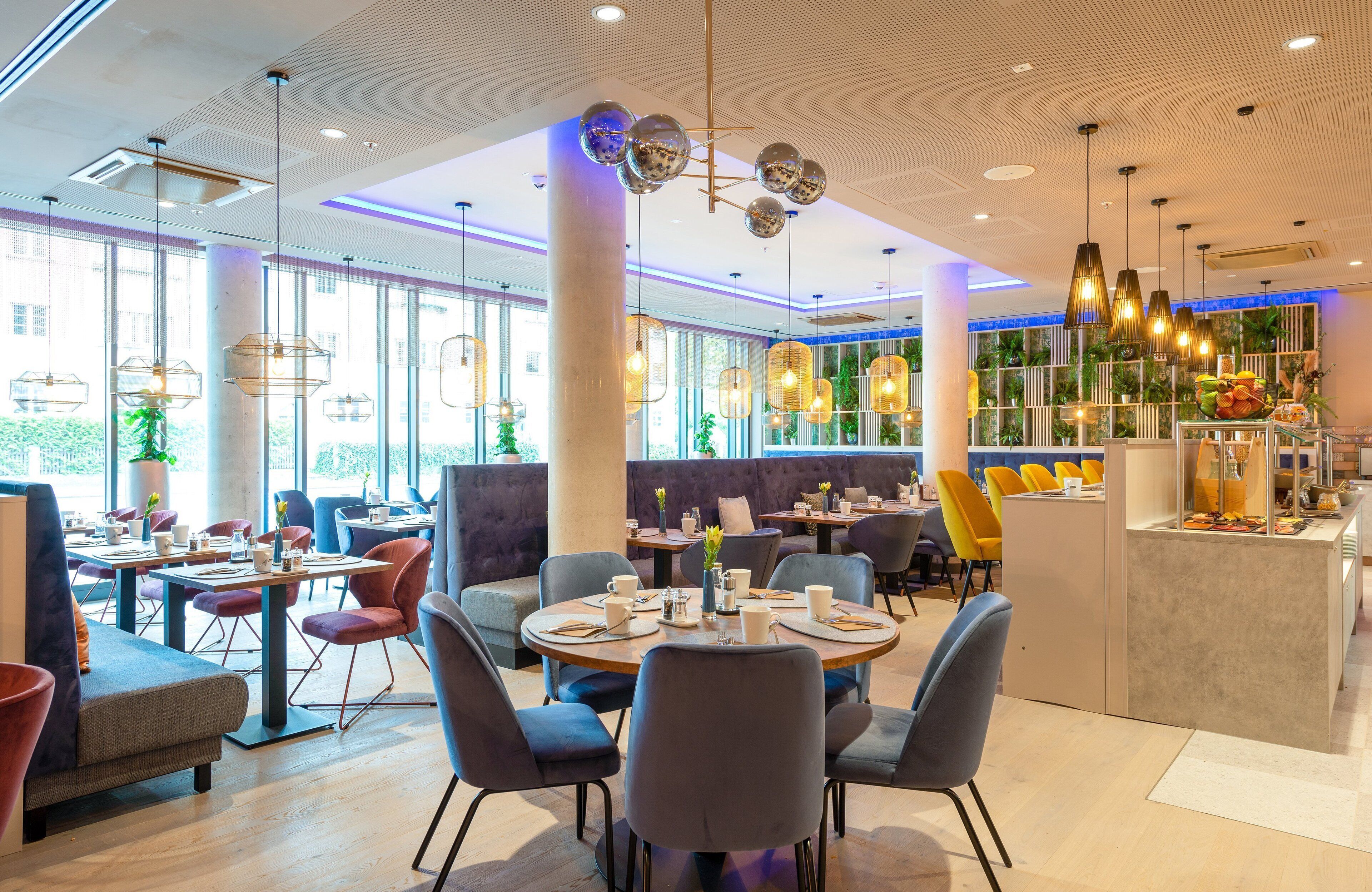 A modern restaurant interior with round tables, comfortable seating, and a variety of pendant lights.