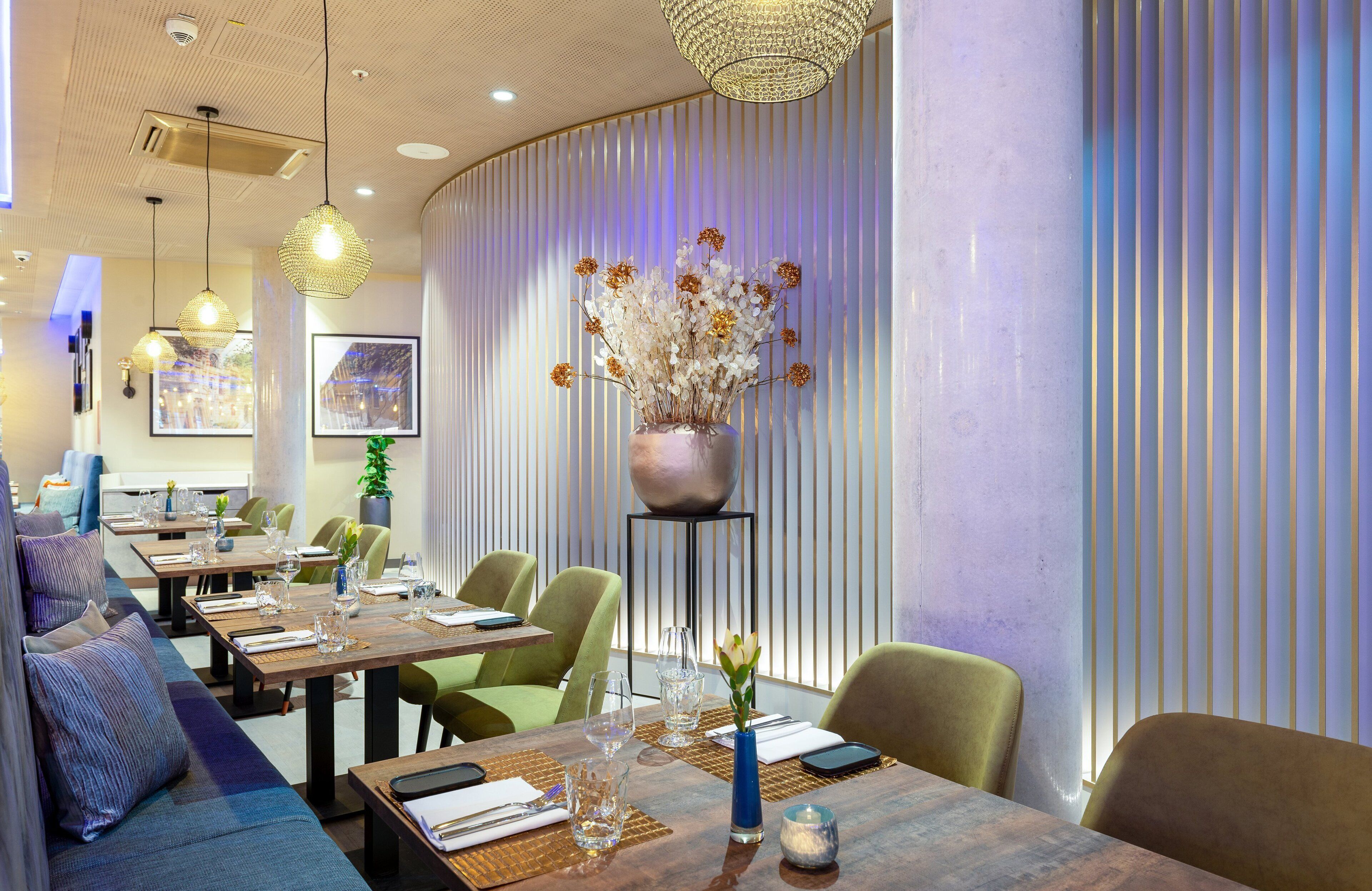 A modern dining area with tables set for two, featuring a vase of flowers and a decorative light fixture.