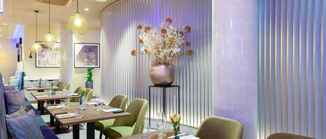 A modern dining area with tables set for two, featuring a vase of flowers and a decorative light fixture.