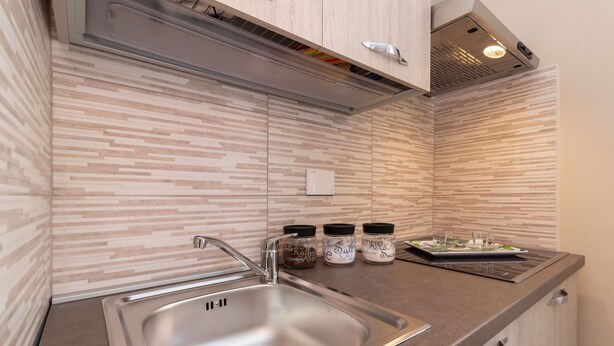 A modern kitchen with a stainless steel sink, wooden cabinets, and a patterned backsplash.