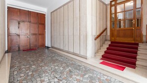 A hallway with a tiled floor, a wooden door, and a staircase with red carpet.