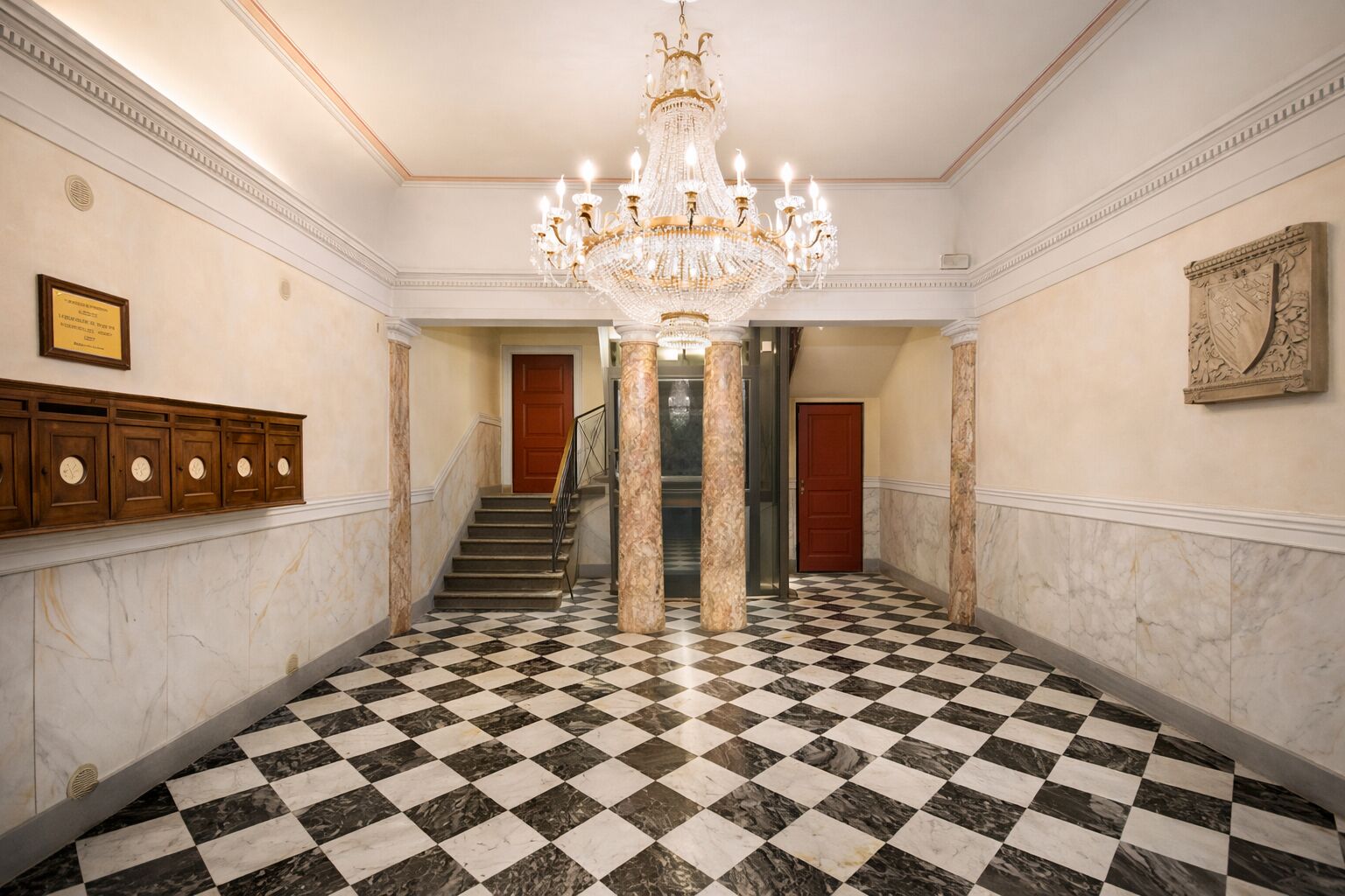A grand hallway with a checkered marble floor, a large chandelier, and a staircase leading to another room.