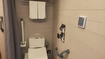 A small, modern bathroom with a toilet, a hand dryer, a paper towel dispenser, and a towel rack with two towels.