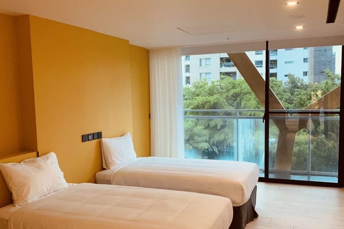 Habitación de hotel con dos camas, un ventanal con vistas a edificios y árboles, y un diseño moderno.