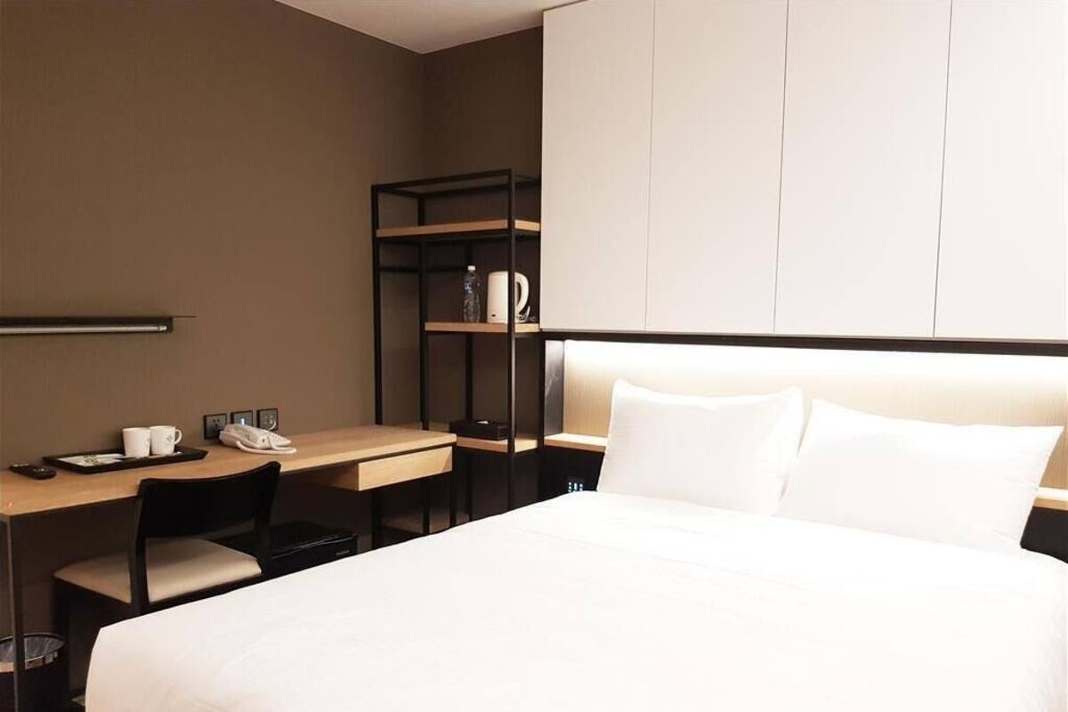 Habitación de hotel con cama, escritorio con silla, teléfono y estante con cafetera.