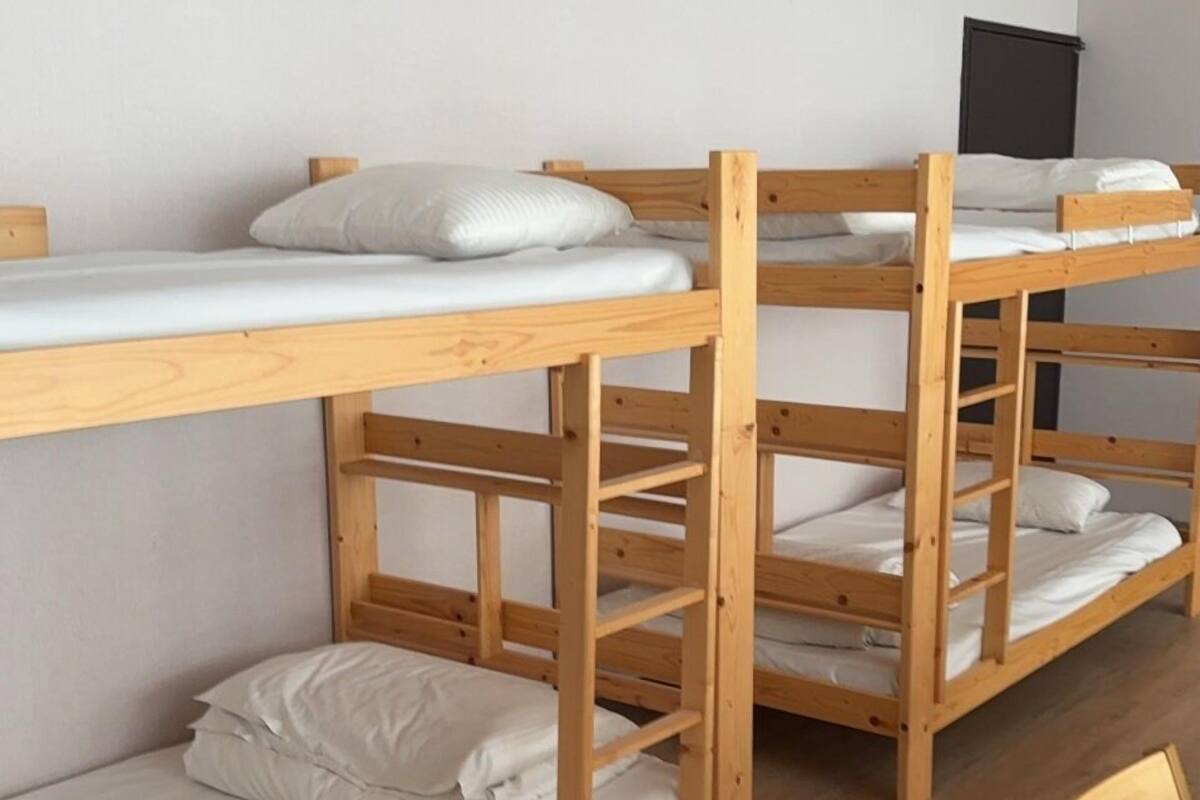 Camas literas con ropa de cama blanca en una habitación con suelos de madera y paredes blancas.