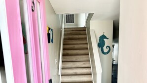 A staircase with wooden steps and a pink door on the left. - Bay views and Sunsets - 4 bedroom in the Heart of Dewey! (Dewey Beach)