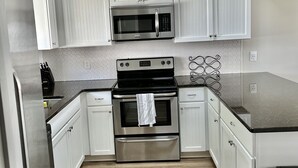 A modern kitchen with white cabinetry, a stainless steel oven, a microwave, and a black countertop. - Bay views and Sunsets - 4 bedroom in the Heart of Dewey! (Dewey Beach)