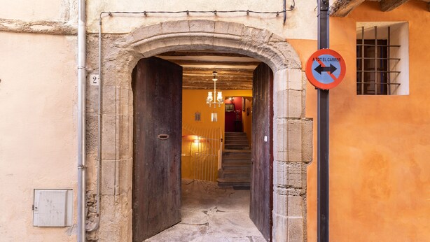 An entrance with a stone archway leading to a staircase, a no parking sign, and a building with a yellow facade. - calamarta_ cultural tourism (Santa Coloma de Queralt)