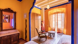 A room with a bed, a wooden dresser, a chair, a table, and a large window with curtains. - calamarta_ cultural tourism (Santa Coloma de Queralt)