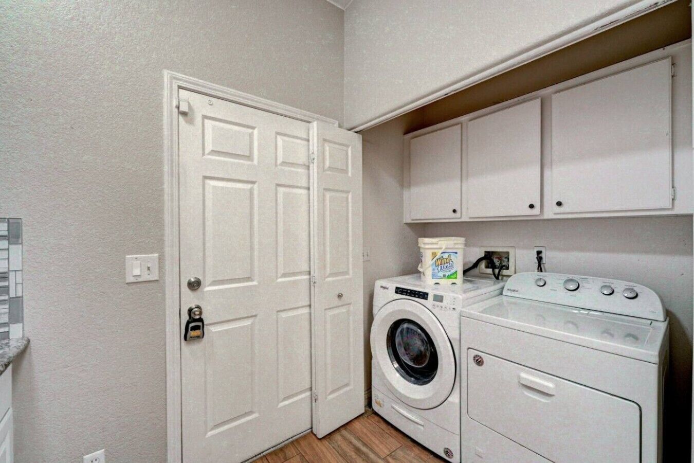Un cuarto de lavandería con lavadora y secadora, un armario sobre la secadora y una puerta con cerradura.