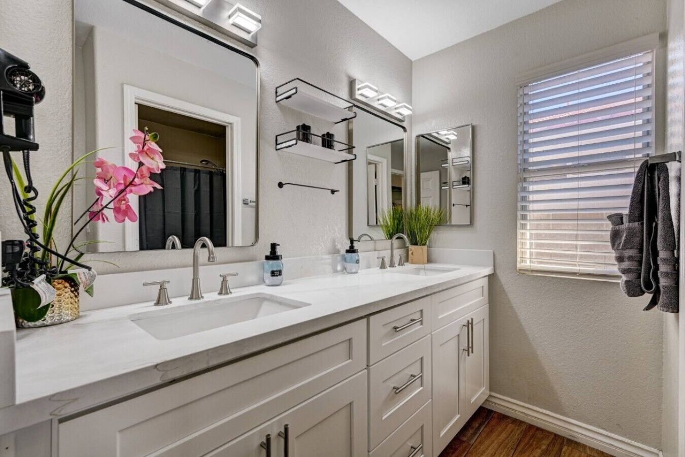A bathroom with a double sink, a large mirror, and a window with blinds.