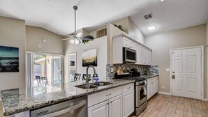 A kitchen with a granite countertop, stainless steel appliances, white cabinetry, and a ceiling fan. - Beautiful Las Vegas home (North Las Vegas)