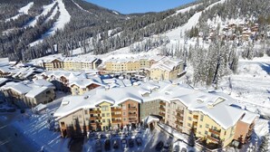 Une station de ski enneigée, avec plusieurs bâtiments, un parking et une piste de ski en arrière-plan.