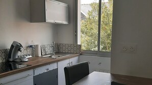 Eine kompakte Küche mit integriertem Mikrowellenherd, Kaffeemaschine und Spüle. Ein Fenster sorgt für natürliches Licht und bietet Blick auf Bäume.