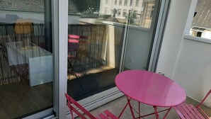 Ein Balkon mit Glastür, einem rosafarbenen Tisch und roten Stühlen.