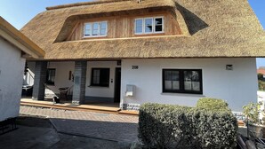 A house with a thatched roof, a wooden porch, and a small garden. - Ferienwohnung Fuchsbau Vitte (Insel Hiddensee)