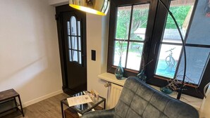 A modern living room with a grey armchair, a small coffee table, and a large window with a view of a bicycle. - Ferienwohnung Fuchsbau Vitte (Insel Hiddensee)